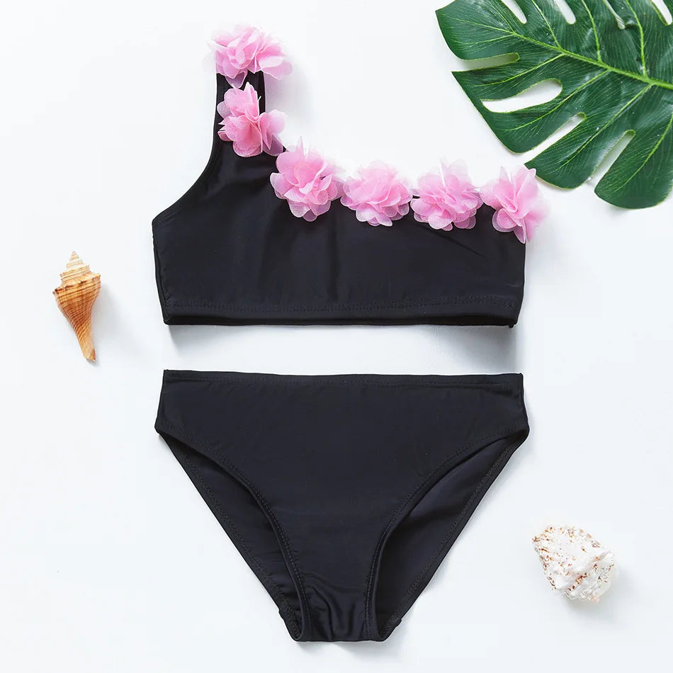Black girls two-piece swimsuit set with pink floral accents and a green tropical leaf in the background