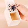 A hand is holding open a white box revealing a black spider inside.