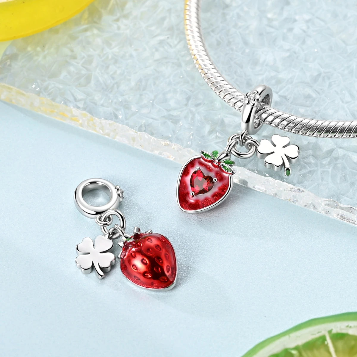 A silver bracelet chain with two fruit charm beads, one shaped like a strawberry and the other like a clover.