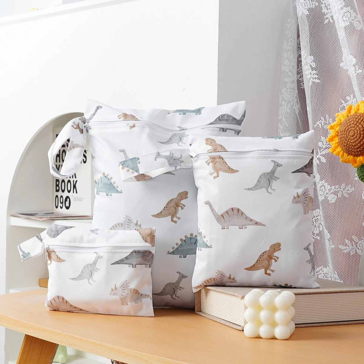 A pack of three white waterproof wet and dry bags for swimsuits, diapers, and travel, featuring dinosaur patterns.