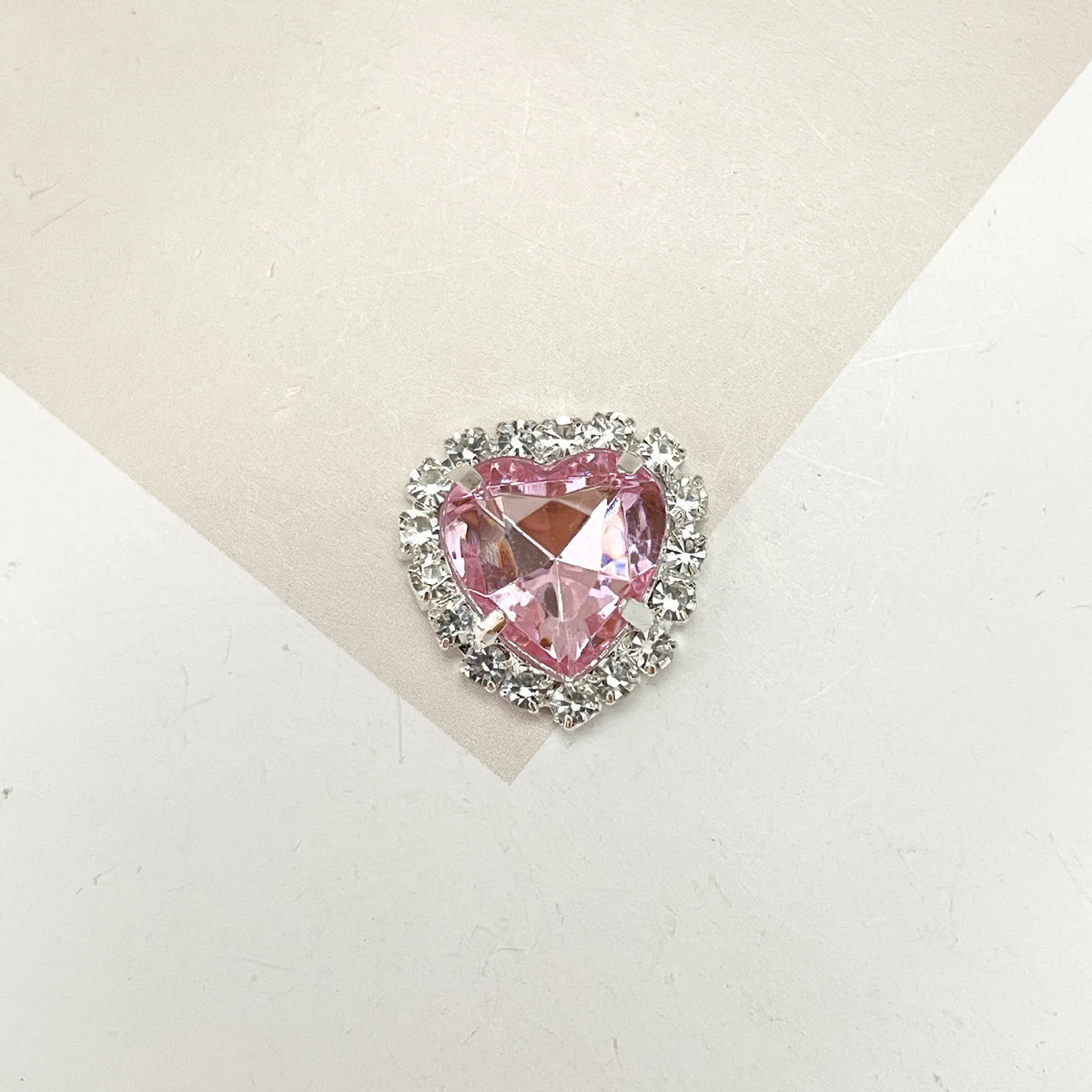 A heart-shaped pink gemstone surrounded by clear rhinestones for DIY crafts.