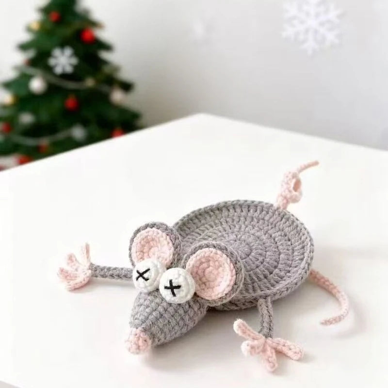 A handmade crochet lizard coaster with funny facial features resting on a white surface.