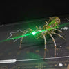 A detailed steampunk metal spider model is illuminated by a bright green laser beam on a dark surface.