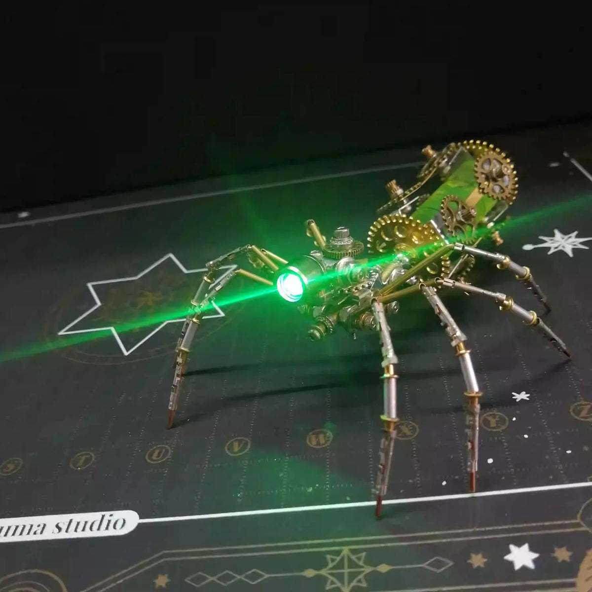 A detailed steampunk metal spider model is illuminated by a bright green laser beam on a dark surface.