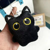 A black cat plush cushion with large yellow eyes is held in a hand against a white background.