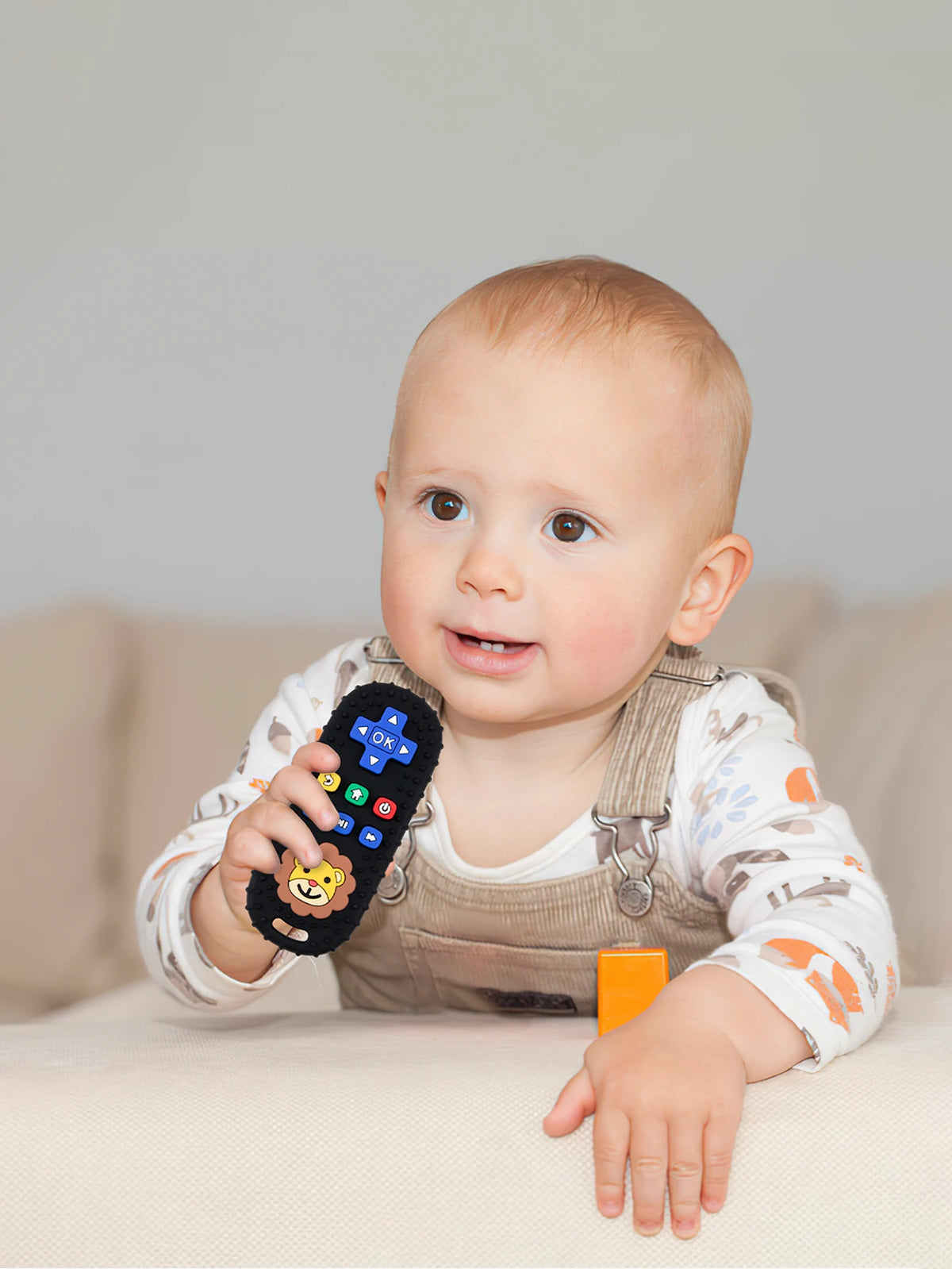 A baby is holding a lion-shaped silicone teether with remote control features.