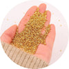 A hand holds a pile of gold metallic glass beads for jewelry making