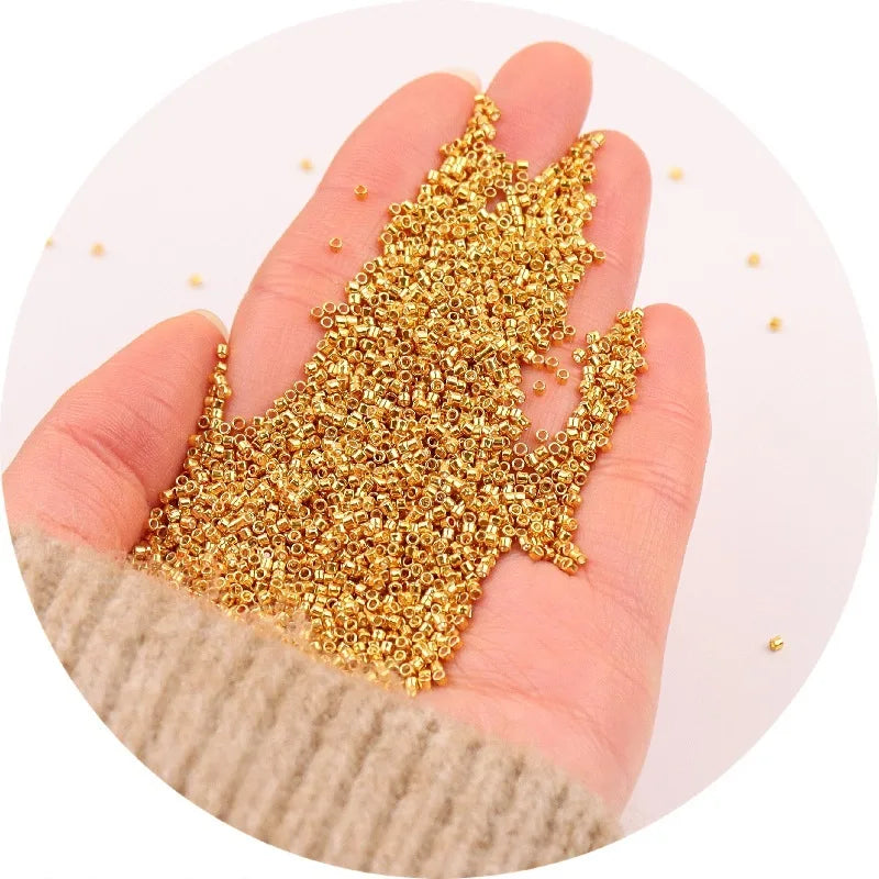 A hand holds a pile of gold metallic glass beads for jewelry making