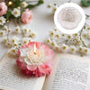A pink floral silicone candle mold surrounded by dried flowers and an open book.