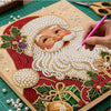 A hand is painting a Christmas Santa face using pearls and beads on a diamond painting canvas.