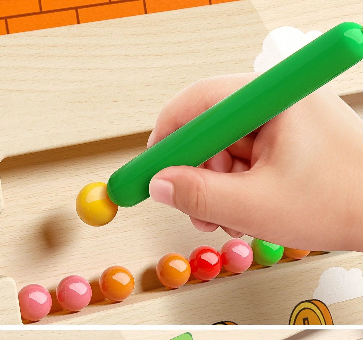 A hand is using a green magnetic color and number maze toy to place colored balls onto a wooden board.