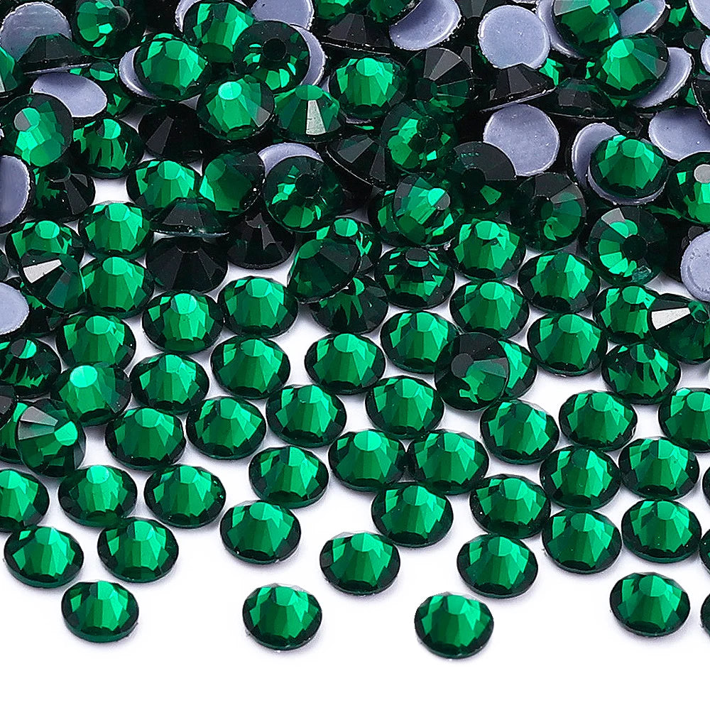 A close-up view of green and dark gray glass crystal rhinestones scattered on a white background.