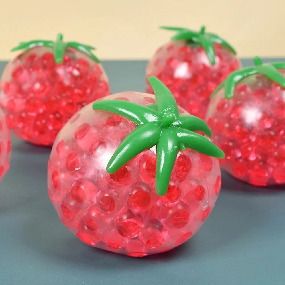 A close-up of a squishy tomato stress relief fidget toy with a glossy red exterior and green stem.