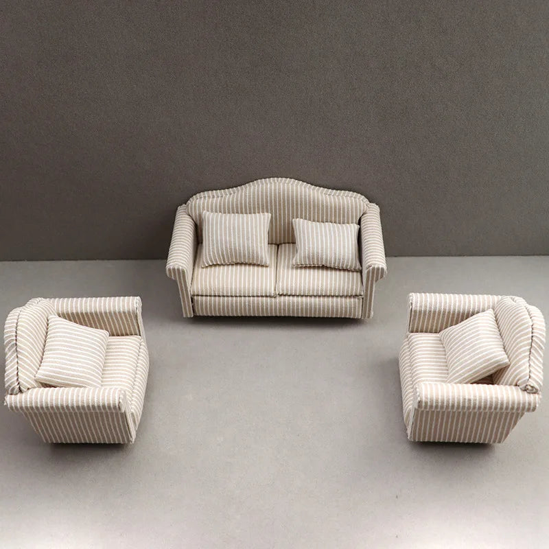 A miniature striped sofa and pillow set for a dollhouse displayed on a gray surface.