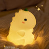 A glowing yellow silicone dinosaur night light resting on a textured fabric.