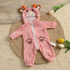 A pink hooded romper featuring a bear face design is laid on a woven mat.