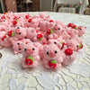 A pile of handmade crochet mini pig keychains in pink and red are displayed on a white lace tablecloth.