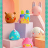 A collection of pink and yellow vinyl figures, including a pig, a rabbit, and a blue creature, displayed on pastel-colored ge
