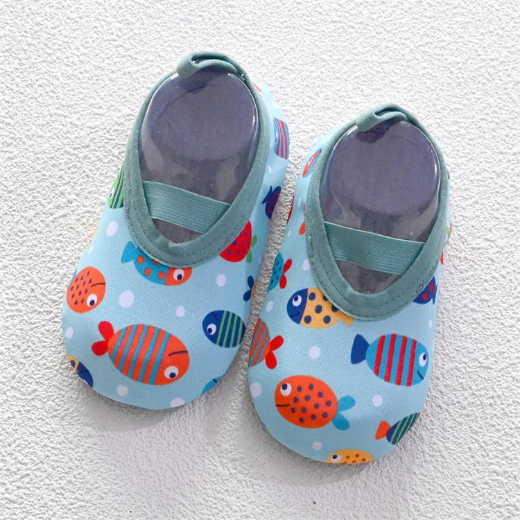 A pair of light blue baby barefoot water shoes decorated with colorful fish patterns and featuring a green strap.