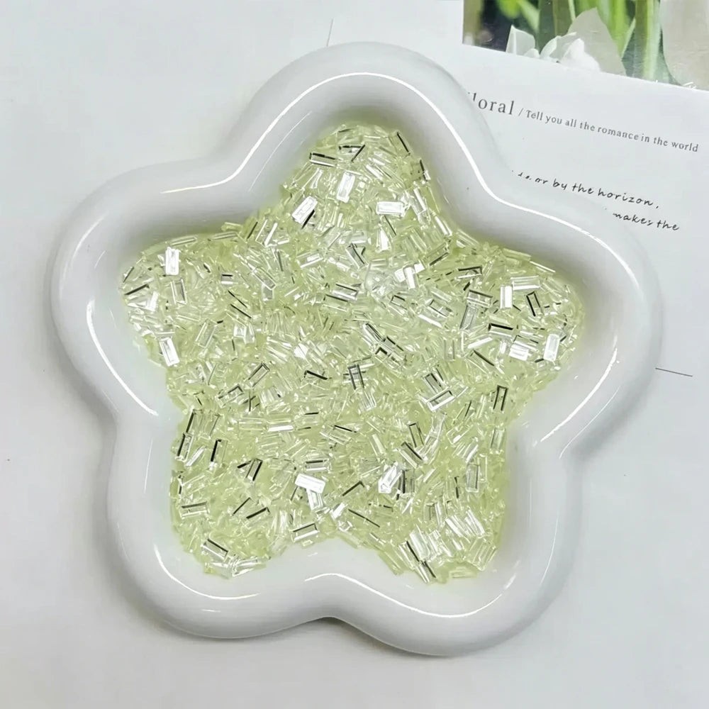 A white, five-pointed mold filled with clear, iridescent green acrylic ice strips for nail art and crafts.