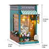 A wooden DIY book nook kit featuring a storefront design with warm LED lighting and striped awning.