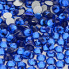 A close-up view of various brilliant blue and clear glass crystal flatback rhinestones scattered on a white surface.