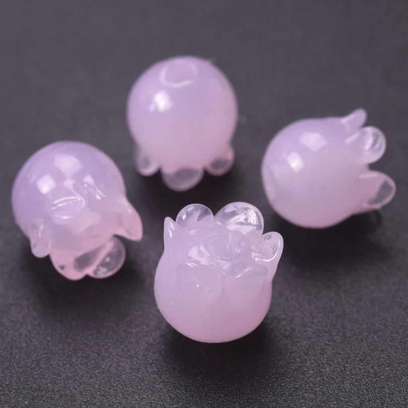 Several translucent pink glass charm pendants shaped like lily of the valley buds are displayed on a dark surface.