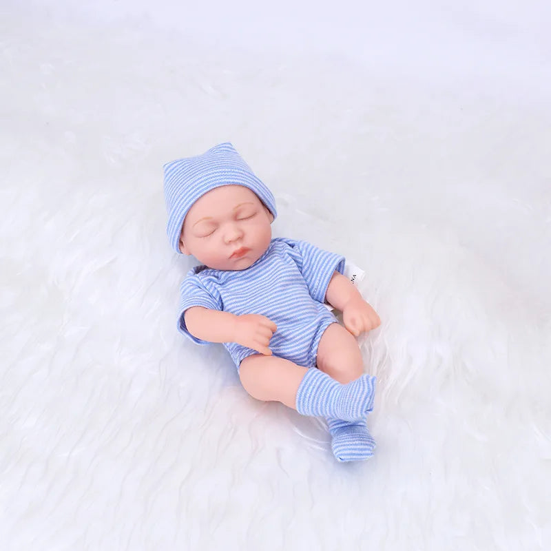 A realistic soft vinyl baby doll wearing a blue striped outfit and matching hat, lying on white fabric.