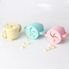 Three silicone snack cups with lids in yellow, teal, and pink colors arranged on a white surface.