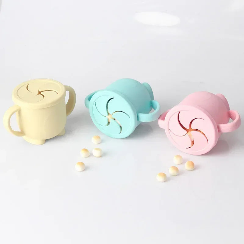Three silicone snack cups with lids in yellow, teal, and pink colors arranged on a white surface.