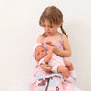 A young girl holds a lifelike vinyl reborn doll with an outfit against a white background.