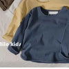 A navy blue long sleeve cotton tee is displayed over a beige shirt on a white surface.