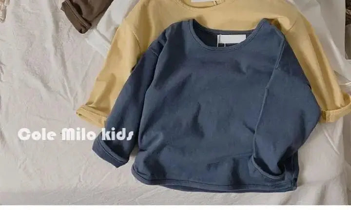 A navy blue long sleeve cotton tee is displayed over a beige shirt on a white surface.
