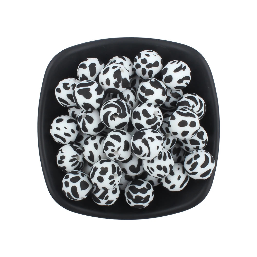 A black bowl filled with small, round, printed silicone beads in leopard and daisy patterns.