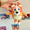 An orange and white plush toy resembling a dog, held by a hand against a background of colorful cards.