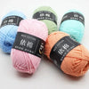 A collection of soft milk cotton yarn in various shades including blue, pink, and orange, packaged with black labels.
