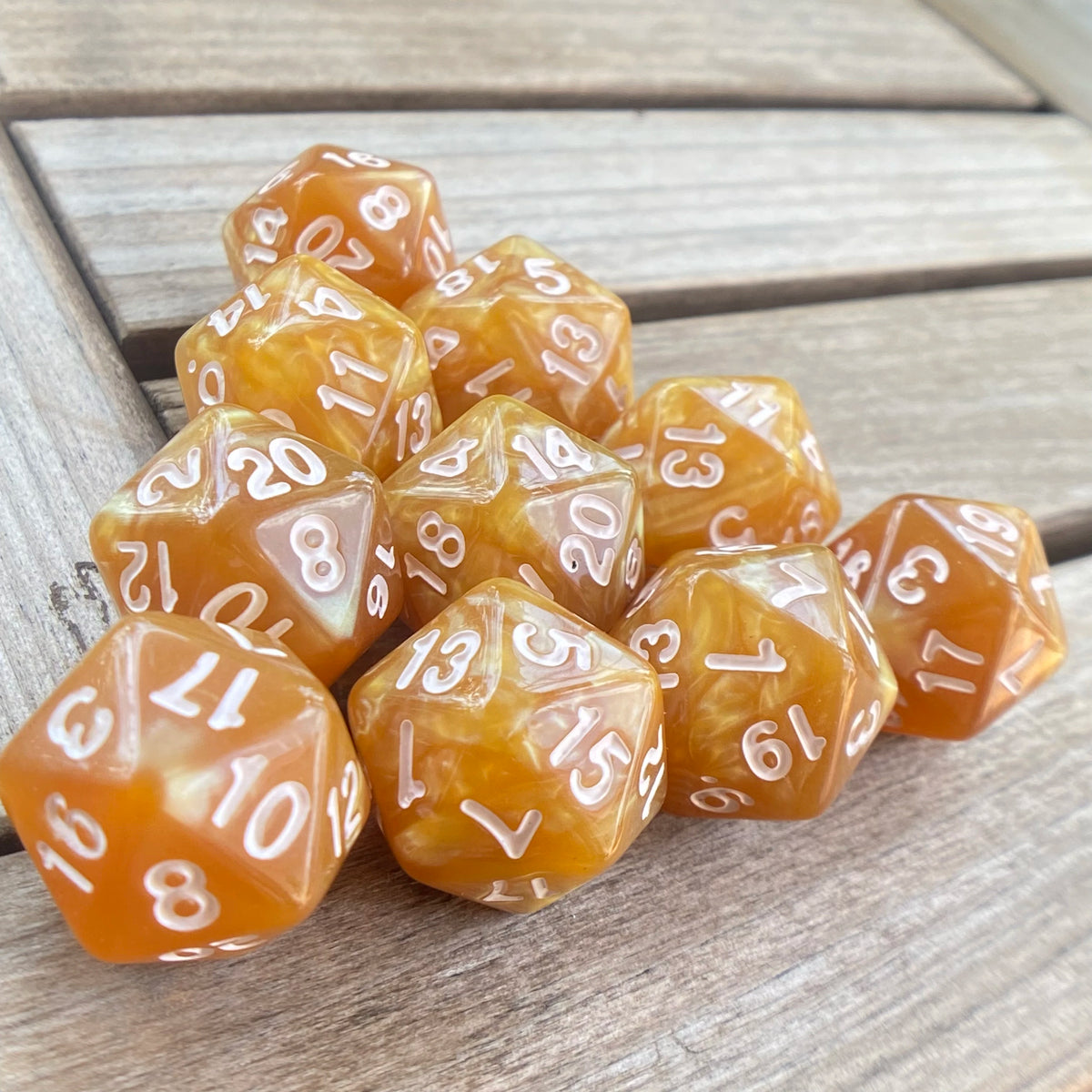 A collection of ten translucent amber acrylic D20 dice arranged on a wooden surface.