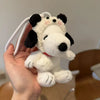 A white and black Snoopy plush keychain charm is held in a hand against a light background.