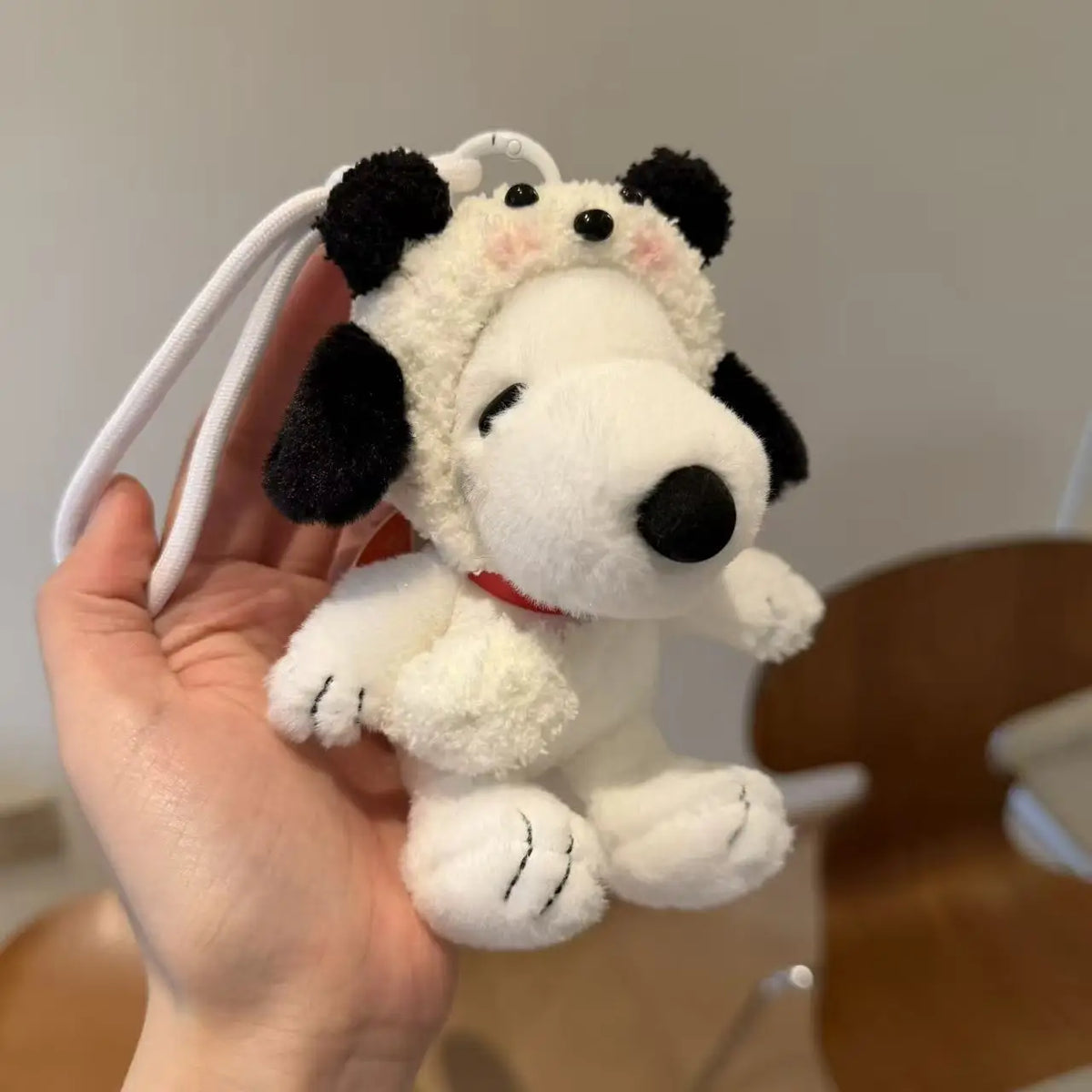 A white and black Snoopy plush keychain charm is held in a hand against a light background.