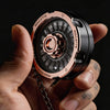 A hand holds a rose gold and black D20 Lucky Roulette fidget spinner with a chain.