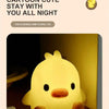A yellow cartoon duck night light emitting warm light on a wooden surface.