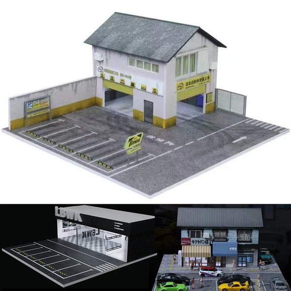 En minigarage-diorama i skala 1:64 med en hvid bygning og en asfaltparkering til legetøjsbiler.