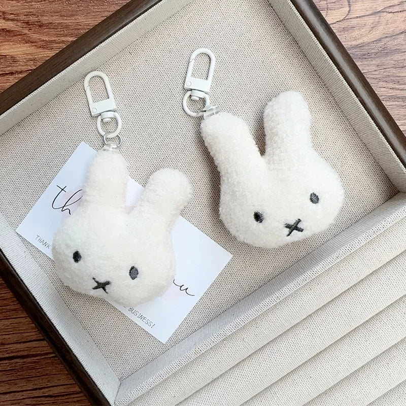 A white Miffy cartoon rabbit keychain pendant hanging from a silver split ring, displayed in a wooden box.