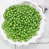 A pile of bright green oval glass rice grain beads for jewelry making displayed in a white dish.