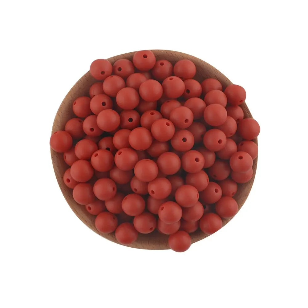 A pile of small, round, reddish-orange silicone beads in a wooden bowl for jewelry making.