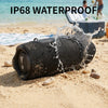 A black portable Bluetooth speaker is shown being splashed by water on a sandy beach.