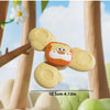 A yellow and orange spinning suction cup bath toy for toddlers is shown against a blurred background of wooden structures and