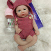 A realistic pink reborn doll with large ears is lying on a white fluffy surface next to a baby bottle.