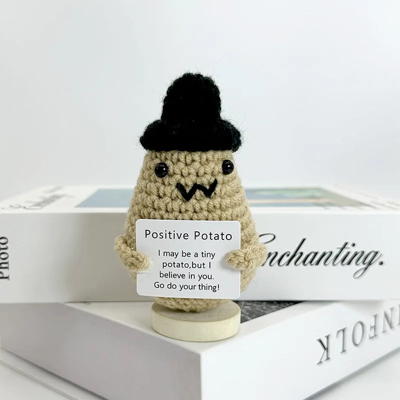 A handwoven crochet ornament shaped like a potato with a black pom-pom hat sitting on a book.