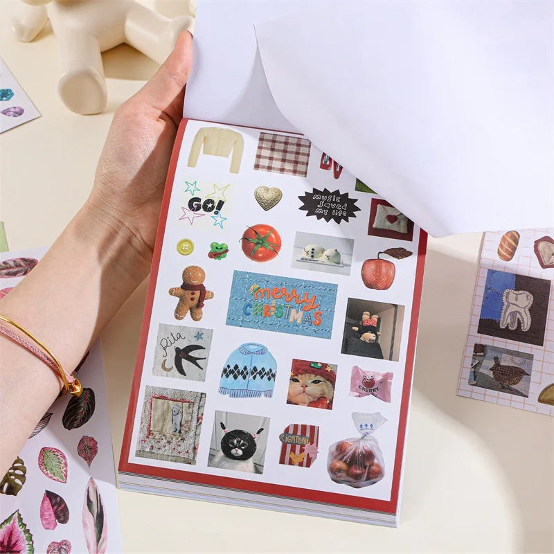A hand holds an open book filled with retro aesthetic stickers for DIY crafting projects.